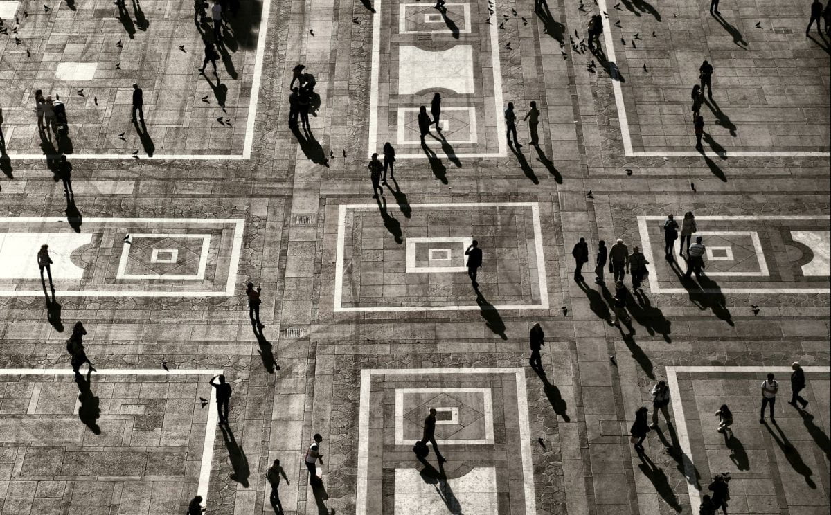 People recognizable only as silhouettes walk across a central square in Europe.